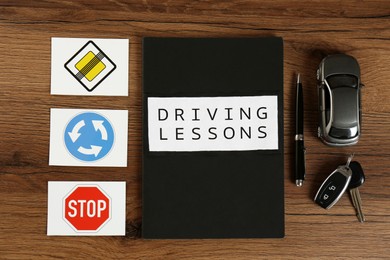 Photo of Flat lay composition with workbook for driving lessons and road signs on wooden background. Passing license exam
