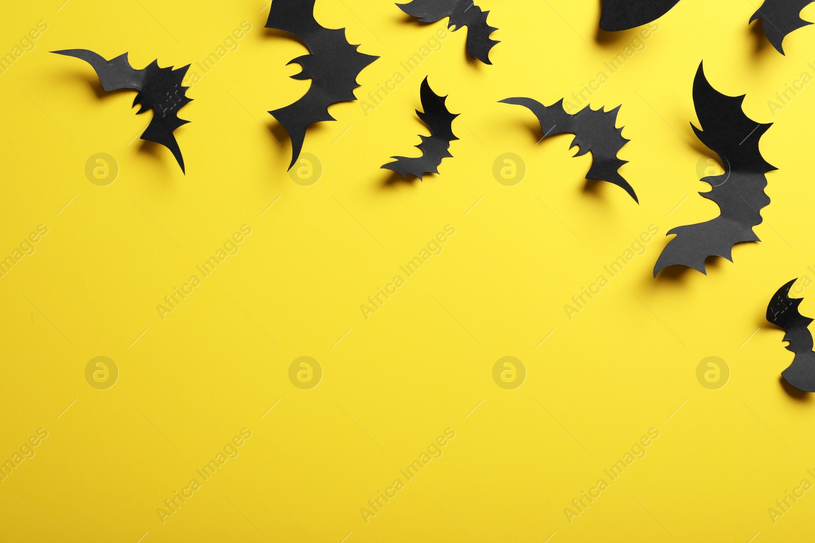 Photo of Paper bats on yellow background, flat lay with space for text. Halloween decor
