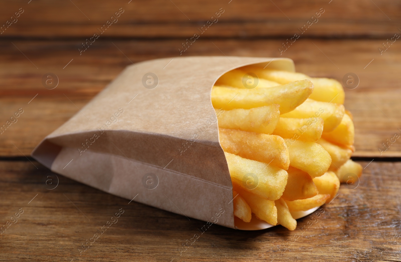 Photo of Delicious french fries in paper box on wooden table, closeup