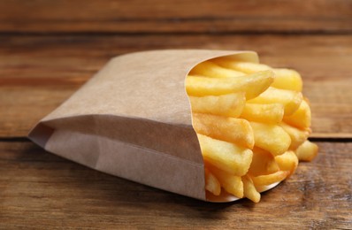 Photo of Delicious french fries in paper box on wooden table, closeup