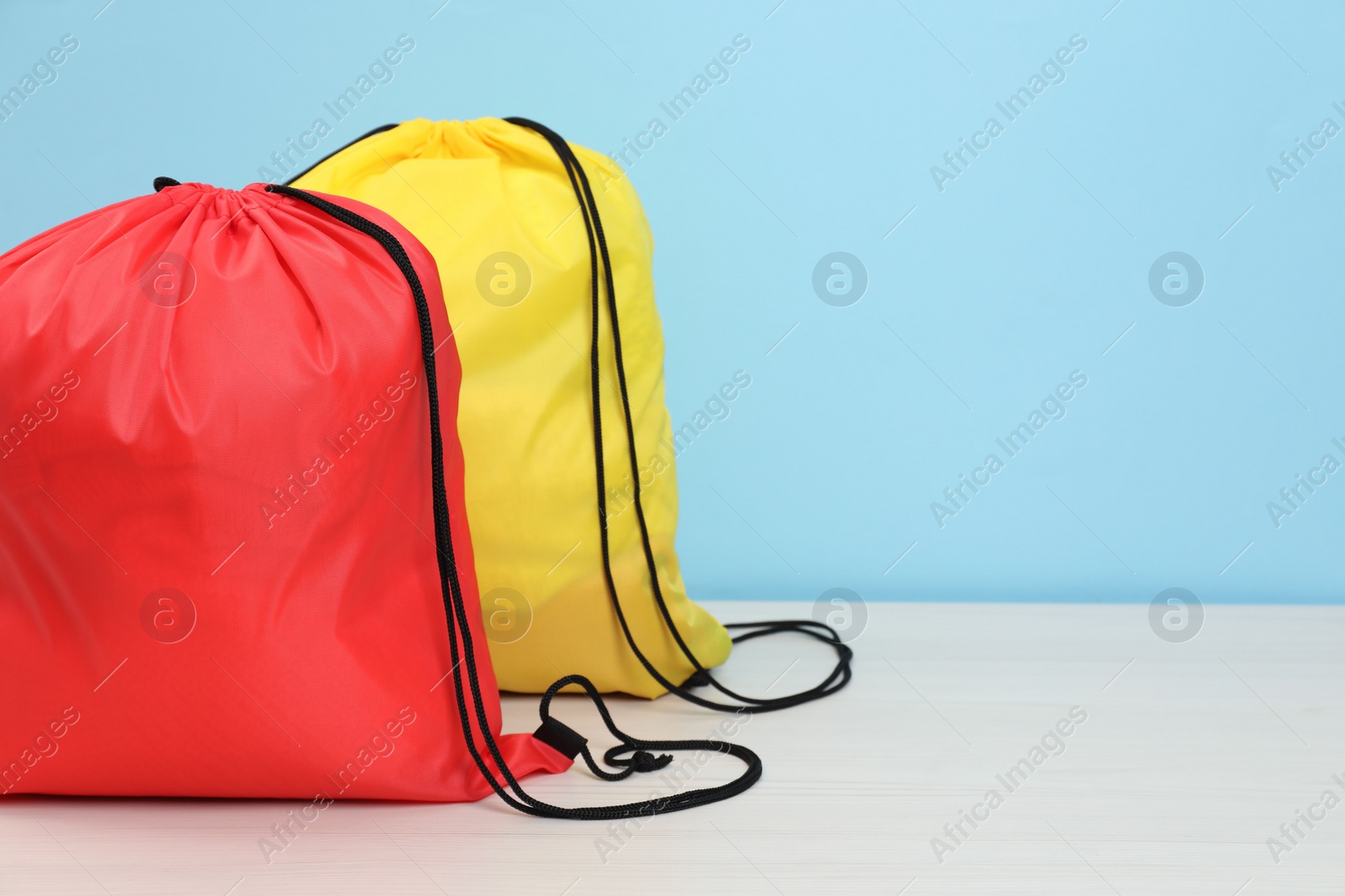 Photo of Two drawstring bags on white wooden table against light blue background. Space for text