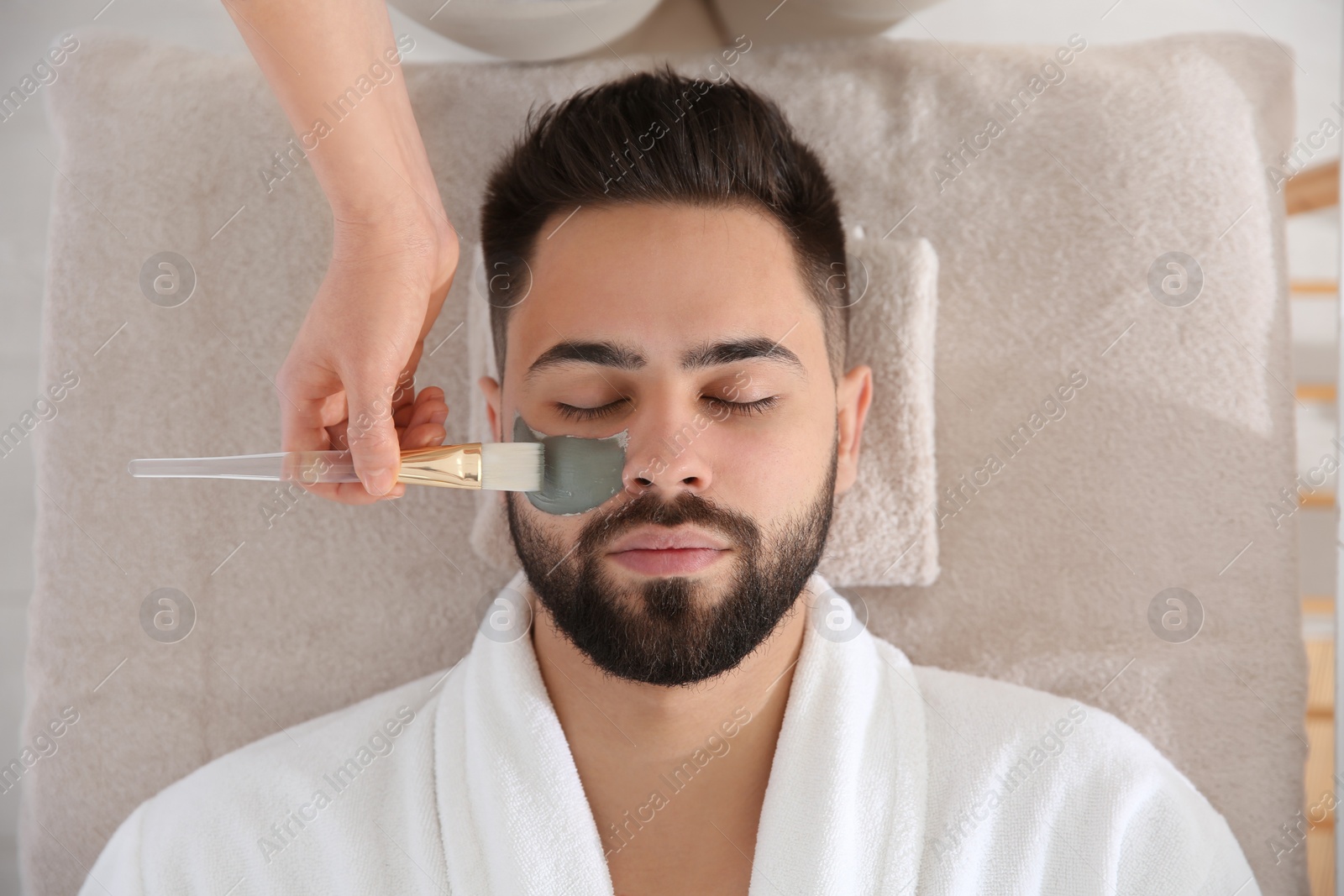 Photo of Cosmetologist applying mask on man's face in spa salon, top view