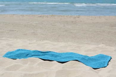 Photo of Soft blue towel on sandy beach near sea, space for text