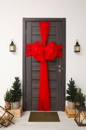 Wooden door with beautiful red bow near evergreen trees ,logs and lanterns. Christmas decoration