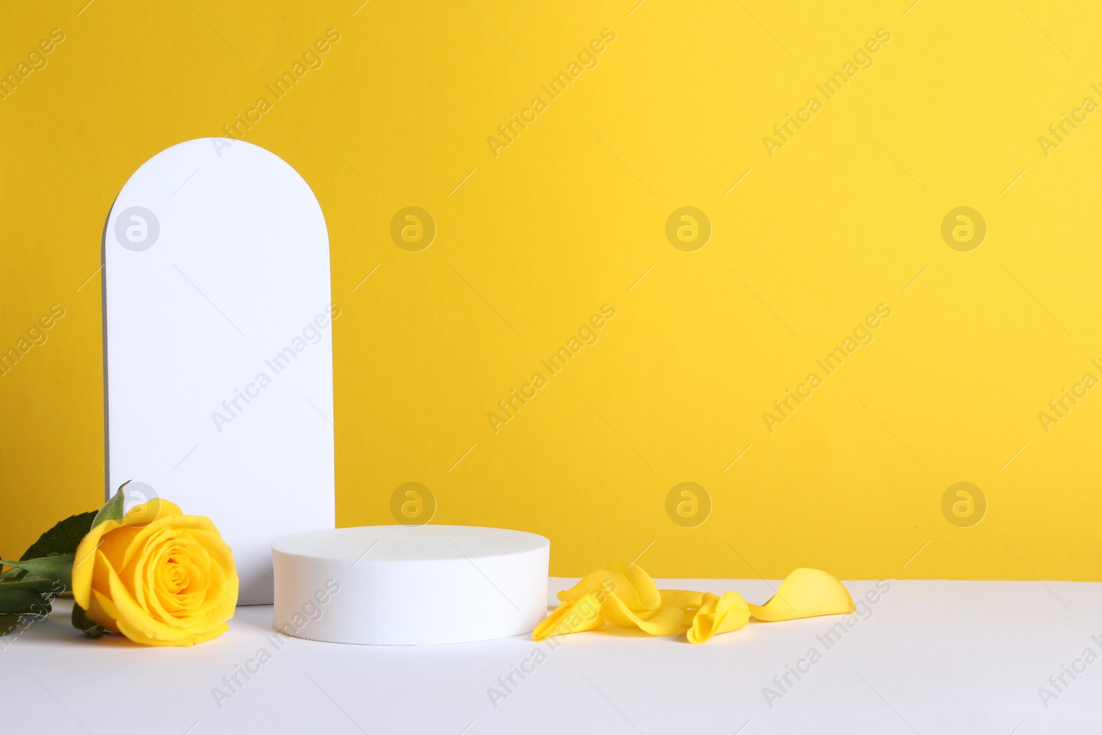 Photo of Beautiful presentation for product. Geometric figures and rose on white table against yellow background, space for text