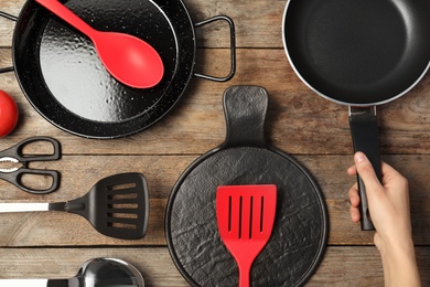 Woman holding frying pan over table with clean cookware, top view