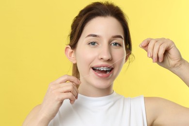 Smiling woman with braces cleaning teeth using dental floss on yellow background