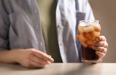 Woman holding glass of cola with ice at table, closeup