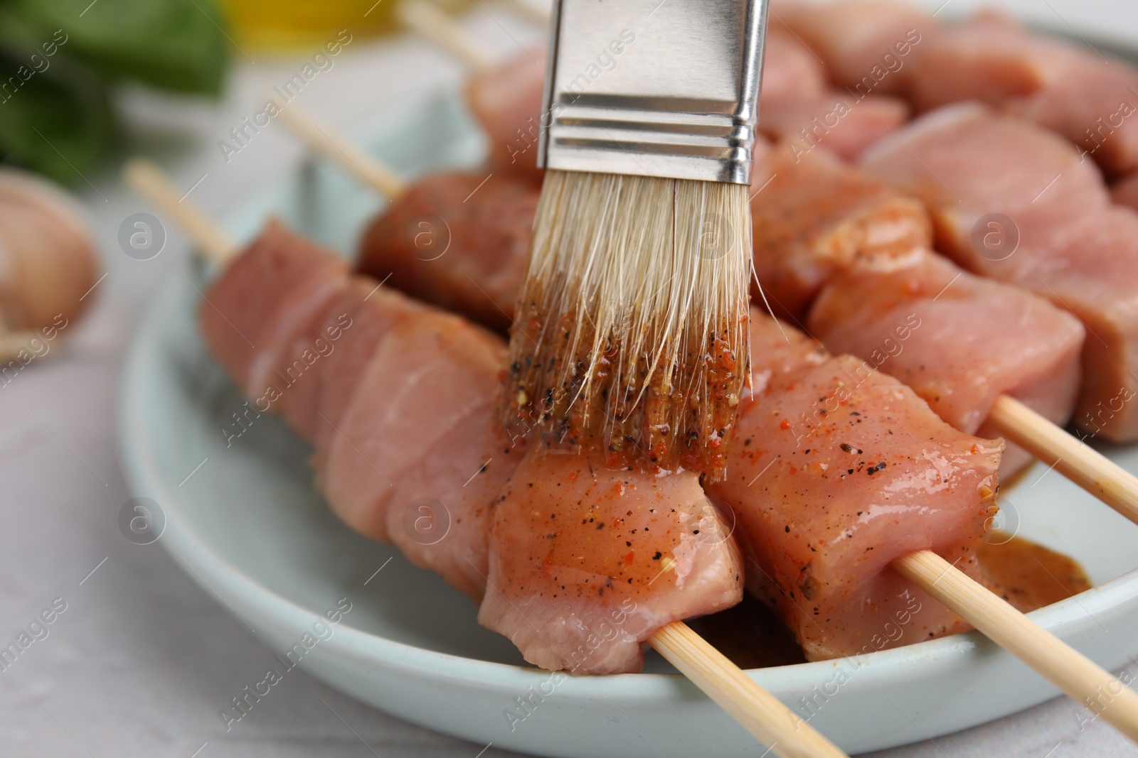 Photo of Spreading marinade onto raw meat with basting brush on light table, closeup