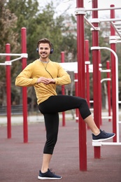 Young man with headphones listening to music and exercising on sports ground