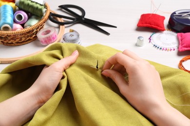 Photo of Woman with sewing needle and thread embroidering on cloth at white wooden table, closeup