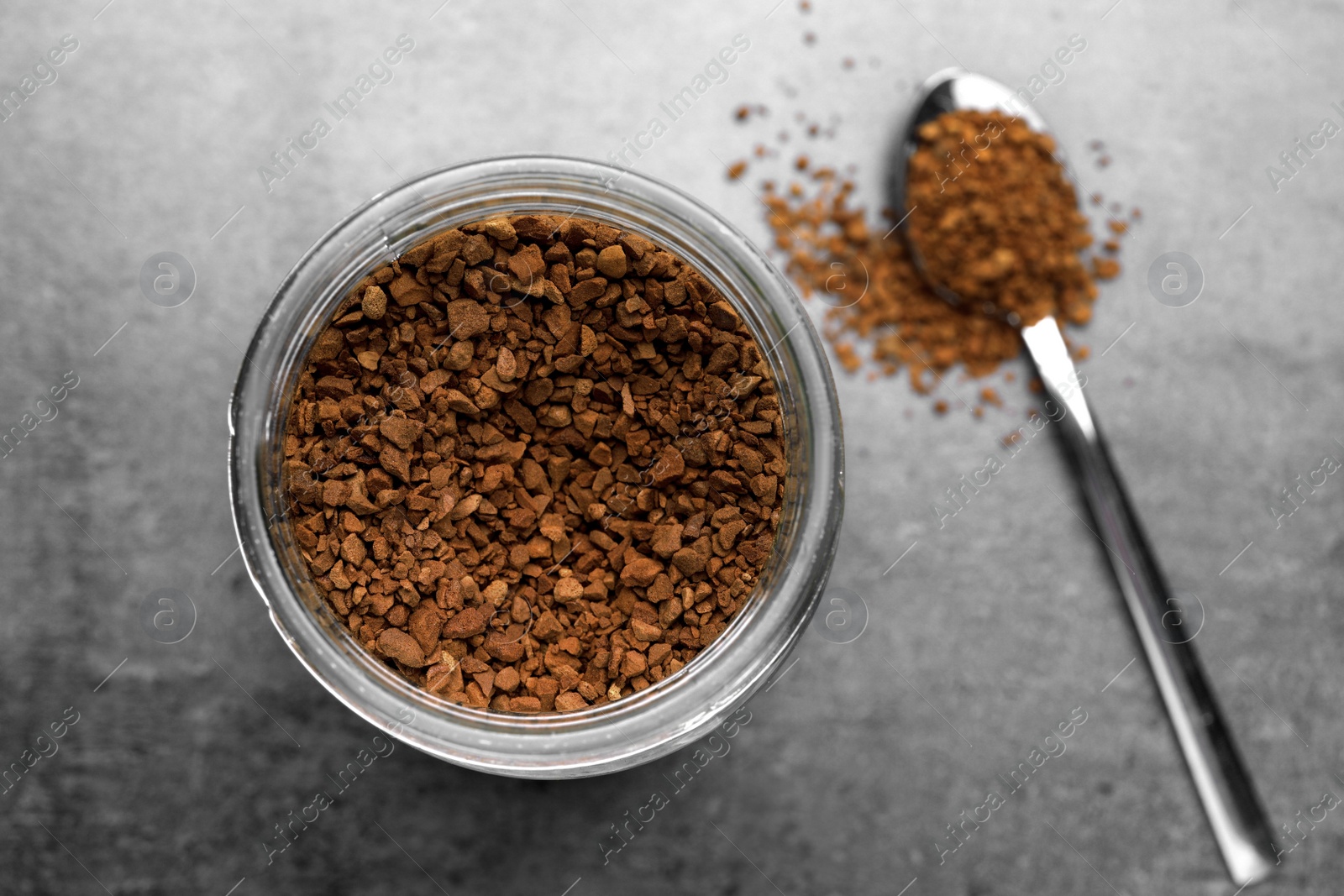 Photo of Spoon and glass jar with instant coffee on grey table, flat lay