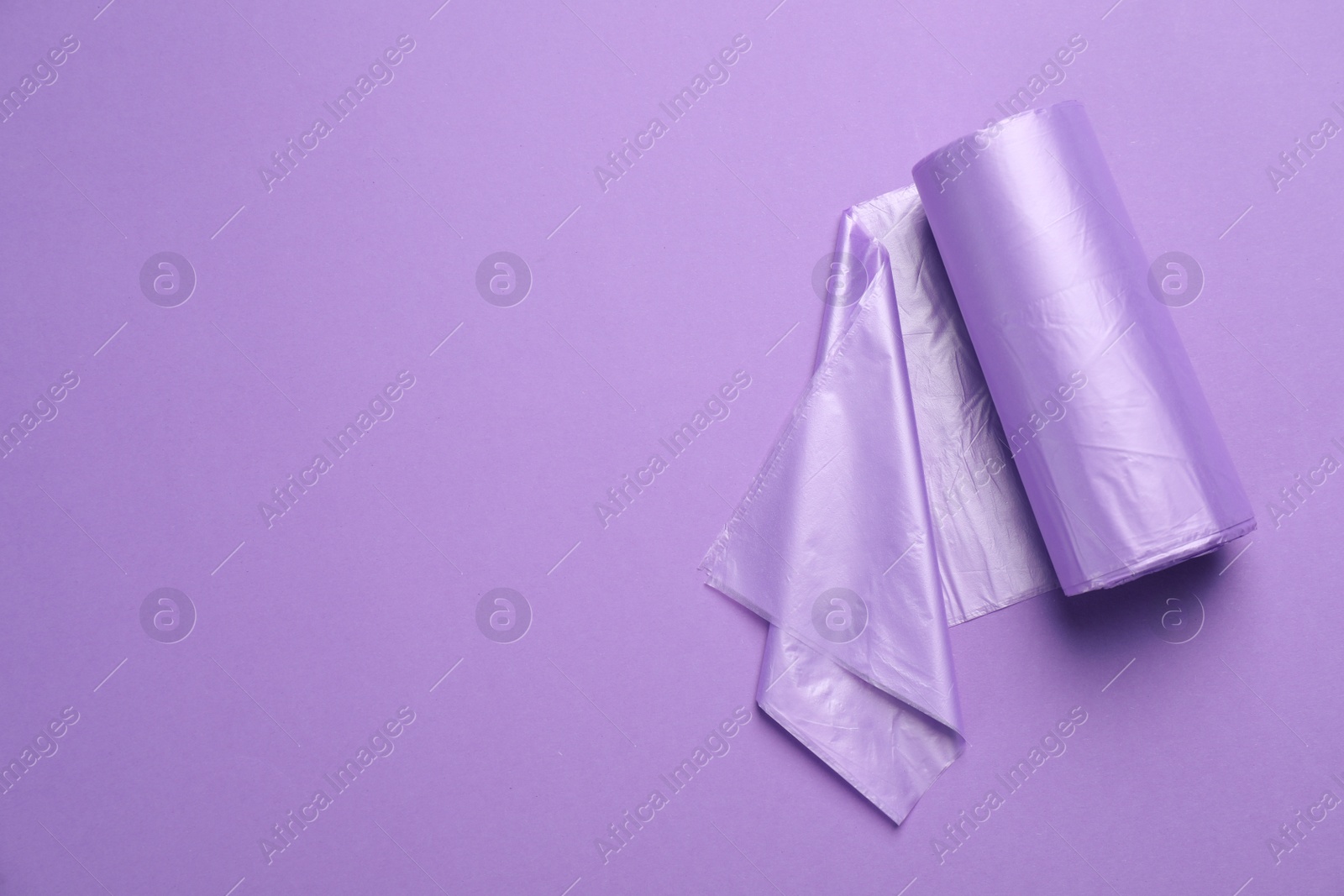Photo of Roll of color garbage bags on violet background, top view. Space for text