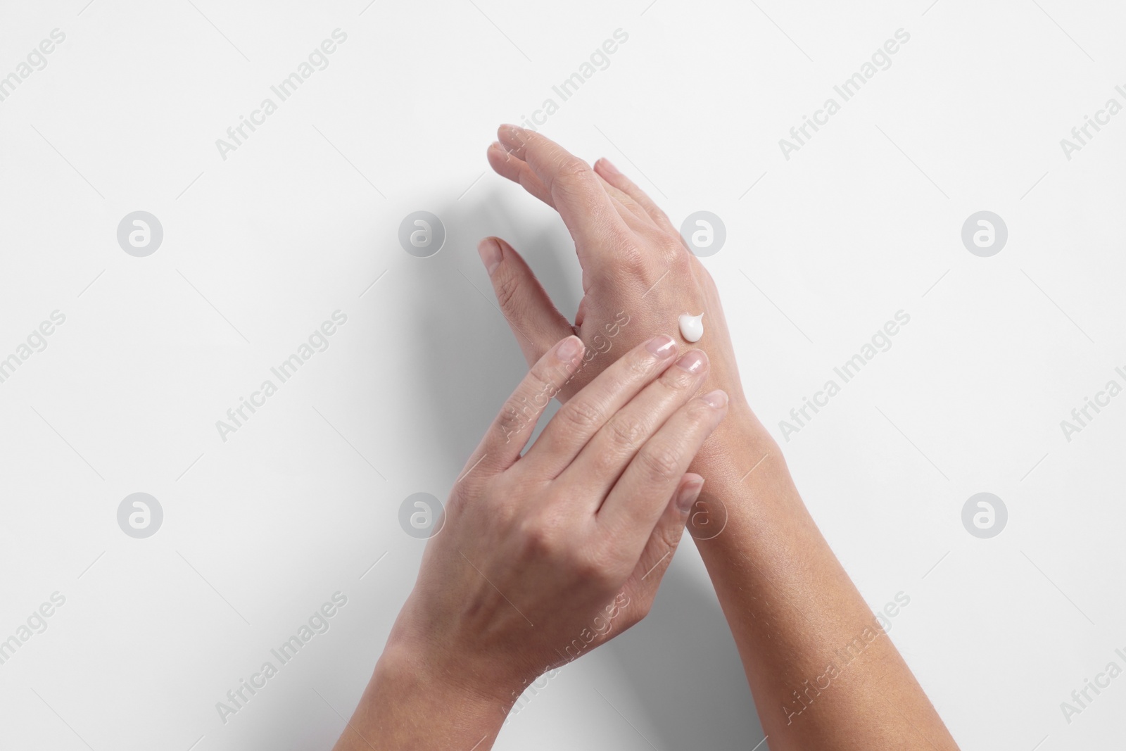 Photo of Woman applying cosmetic cream onto hand on white background, top view