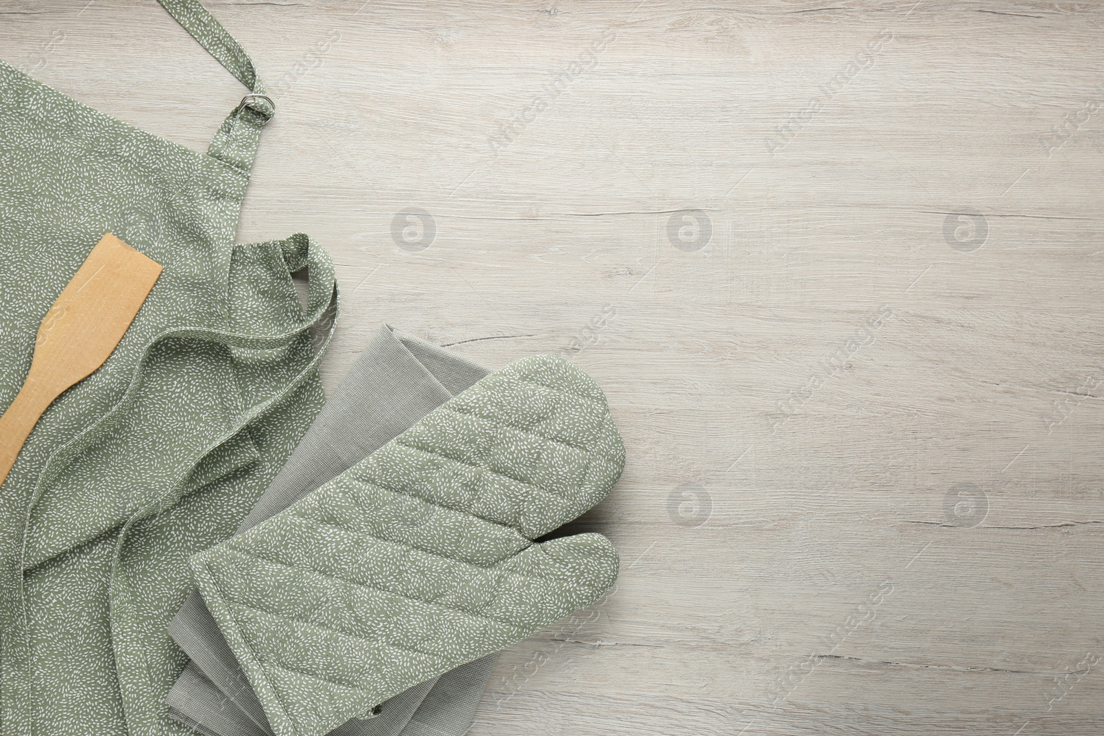 Photo of Kitchen napkin, apron, glove and spatula on wooden table, flat lay. Space for text