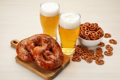 Photo of Tasty pretzels, crackers and glasses of beer on white wooden table