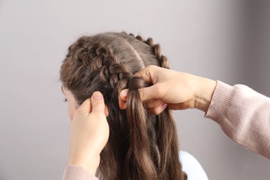 Photo of Professional stylist braiding woman's hair on grey background, closeup