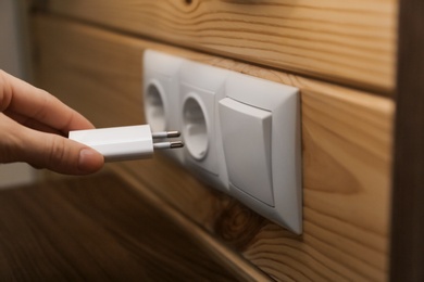 Photo of Woman putting charging plug with USB cable into socket on wall, closeup