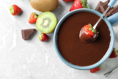 Photo of Dipping strawberry into fondue pot with chocolate on light grey marble table, top view. Space for text