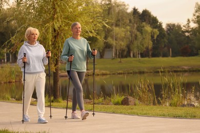 Photo of Two senior friends performing Nordic walking outdoors, space for text