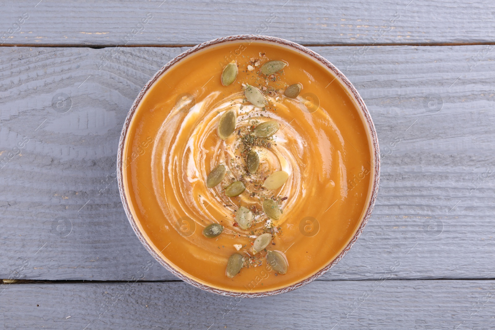 Photo of Bowl of delicious pumpkin soup with seeds and cream on grey wooden table, top view