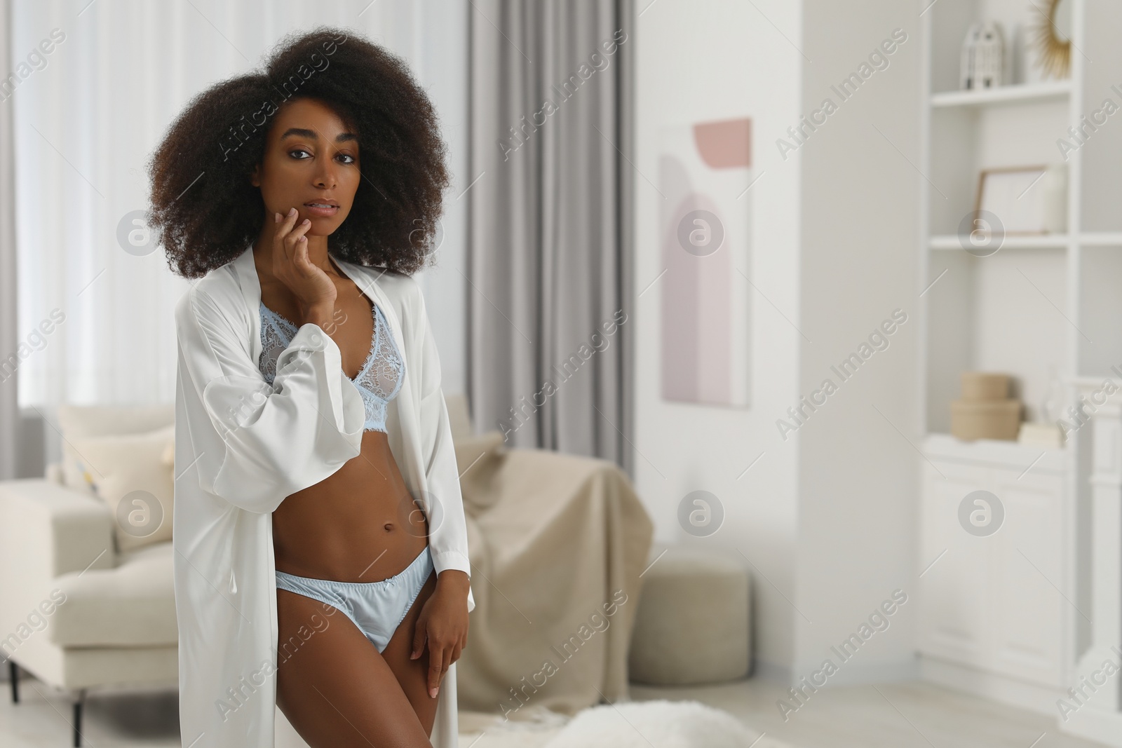 Photo of Beautiful woman in elegant light blue underwear and robe indoors, space for text