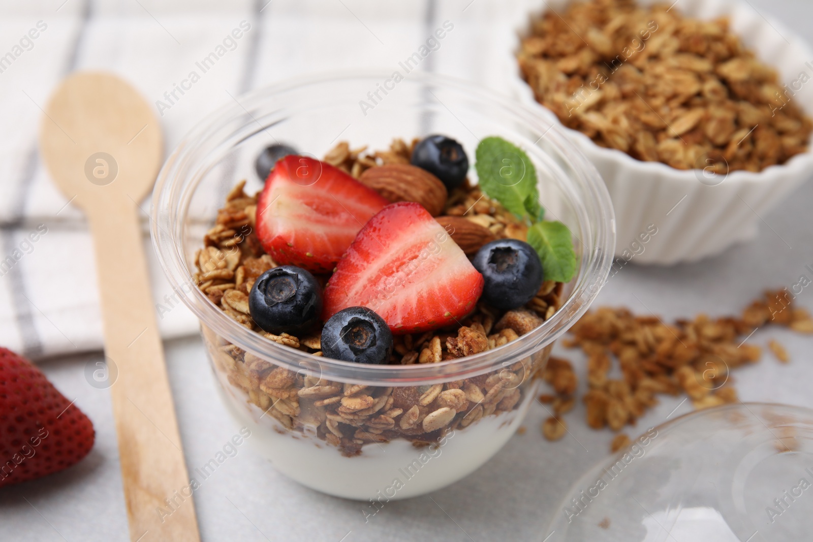 Photo of Tasty granola with berries, nuts and yogurt in plastic cup on light table, closeup