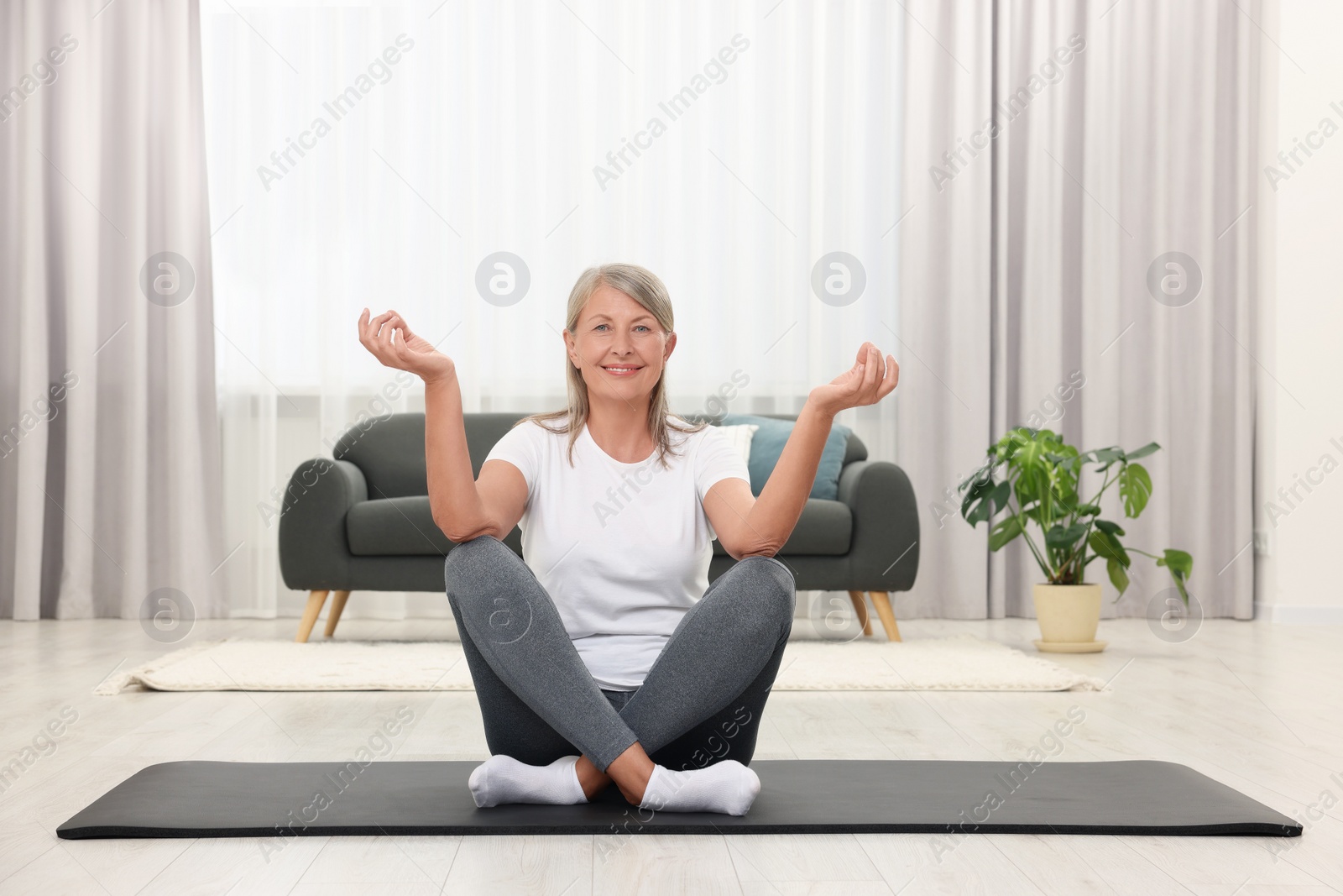 Photo of Happy senior woman practicing yoga on mat at home