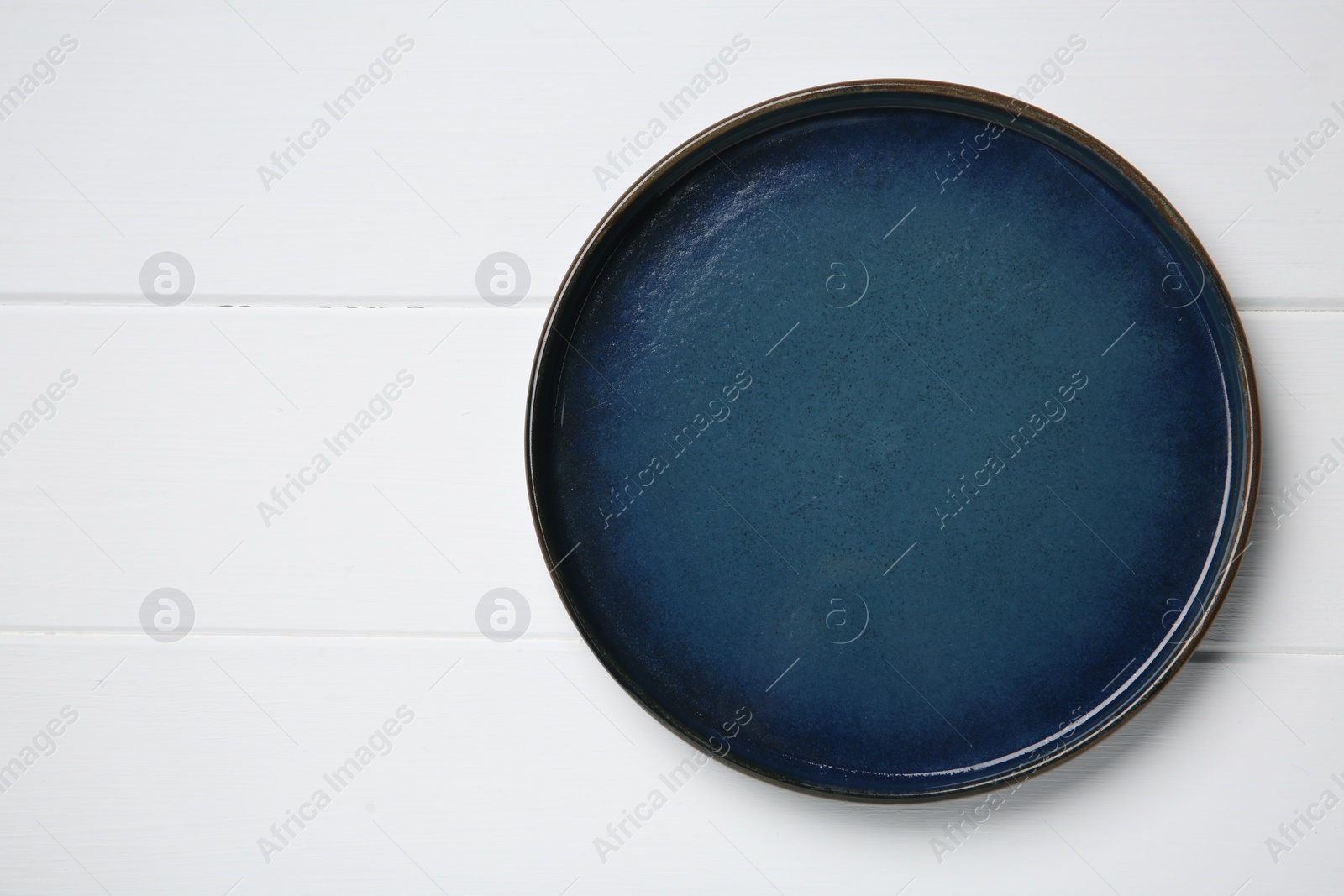 Photo of One dark blue ceramic plate on white wooden table, top view. Space for text