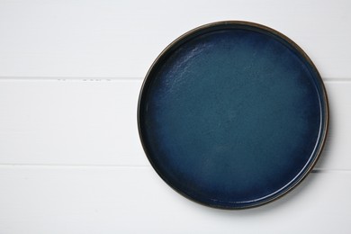 Photo of One dark blue ceramic plate on white wooden table, top view. Space for text