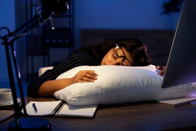 Photo of Tired overworked businesswoman napping with pillow at night in office