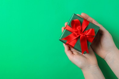 Photo of Woman holding beautifully wrapped Christmas gift box on green background, top view. Space for text