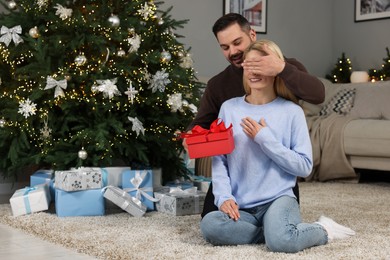 Happy man surprising his woman with Christmas gift at home