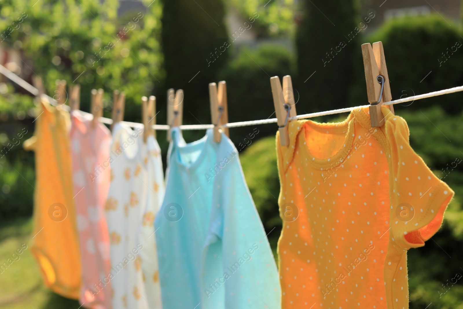 Photo of Clean baby onesies hanging on washing line in garden, closeup. Drying clothes