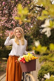 Beautiful young woman with bicycle and flowers in park on pleasant spring day