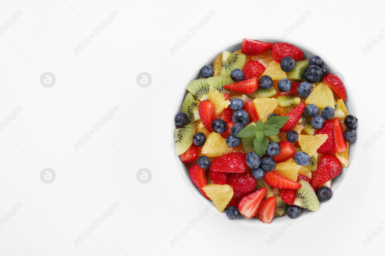 Photo of Yummy fruit salad in bowl on white background, top view. Space for text