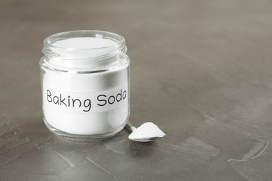 Photo of Jar and spoon with baking soda on grey table, closeup. Space for text