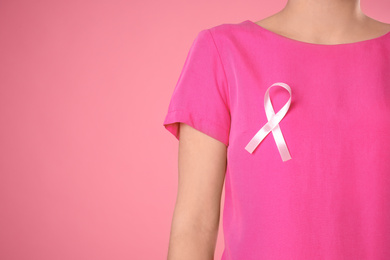 Closeup view of woman with pink ribbon on color background, space for text. Breast cancer awareness