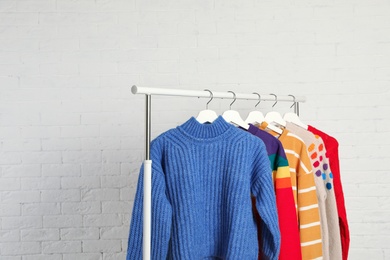 Photo of Collection of warm sweaters hanging on rack against white brick wall