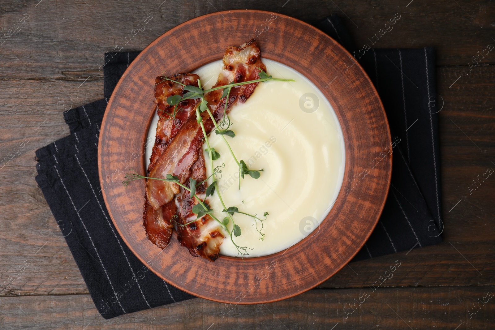 Photo of Delicious potato soup with bacon and microgreens in bowl on wooden table, top view