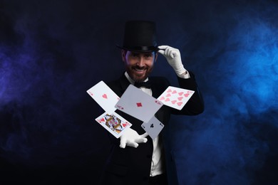 Smiling magician showing trick with cards on dark blue background