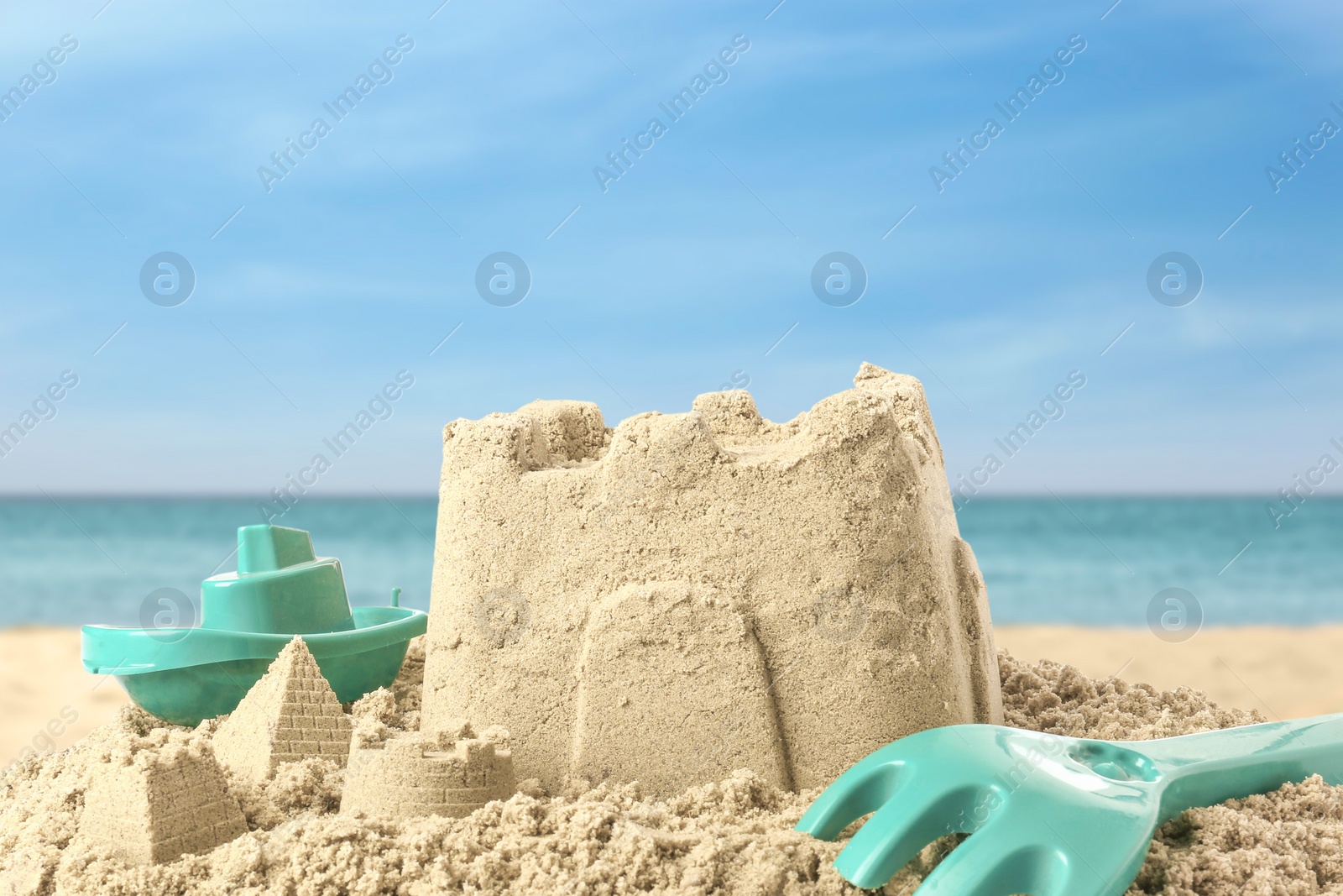 Image of Sand castle with toys on ocean beach, closeup. Outdoor play