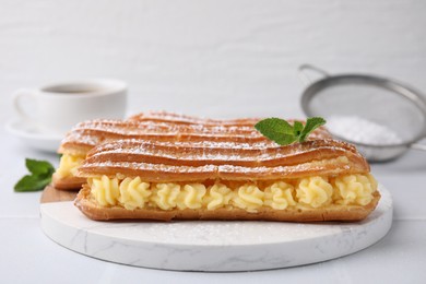 Delicious eclairs filled with cream and mint on white table