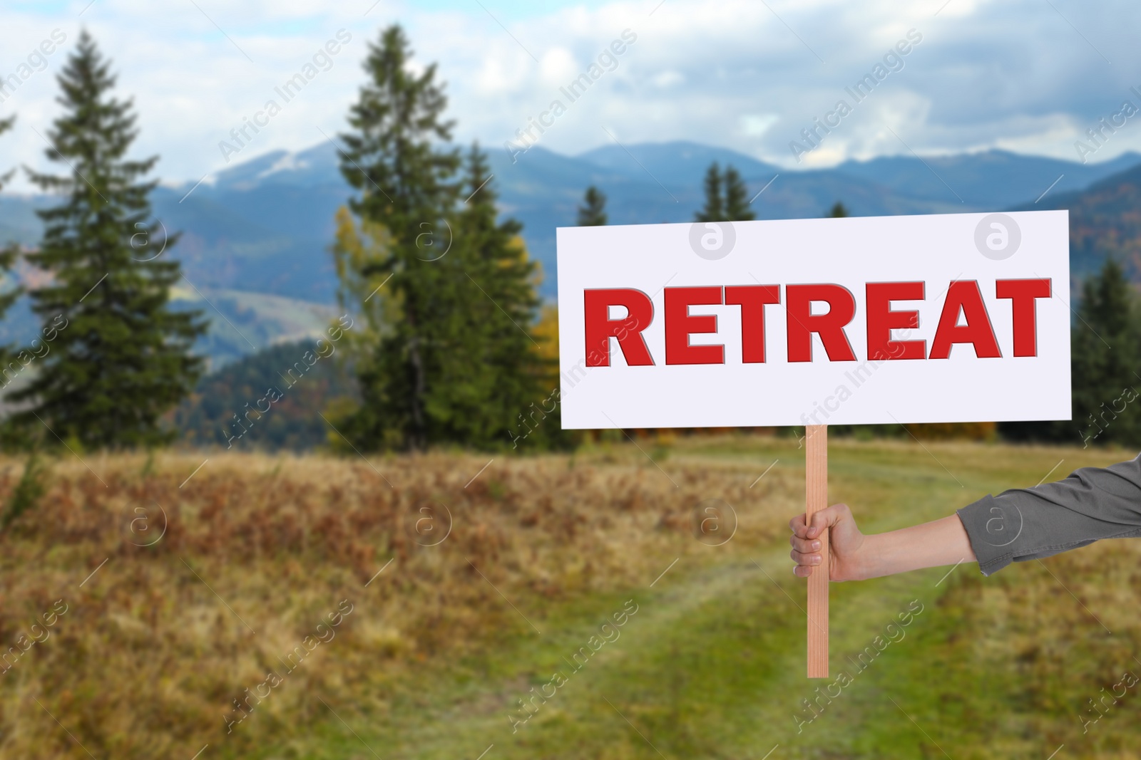 Image of Woman holding wooden sign with word Retreat and beautiful view of mountain landscape