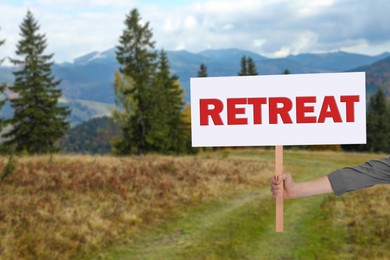 Woman holding wooden sign with word Retreat and beautiful view of mountain landscape