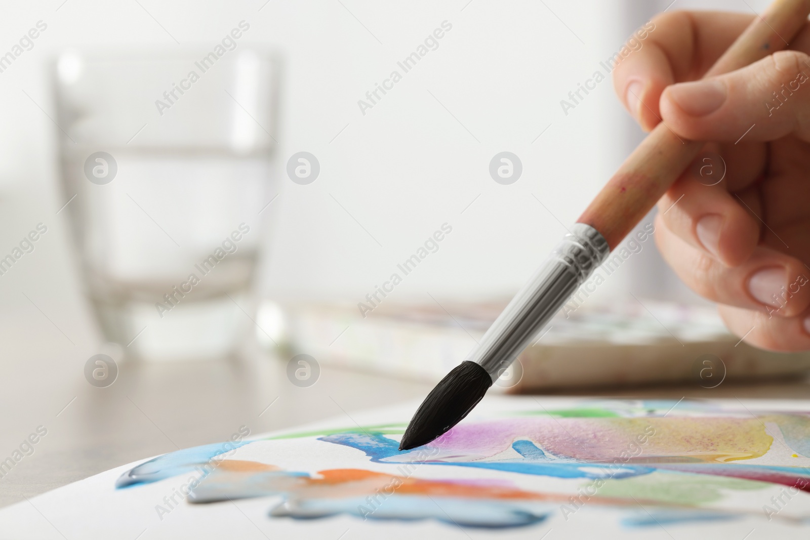Photo of Woman painting with watercolor at wooden table indoors, closeup. Space for text
