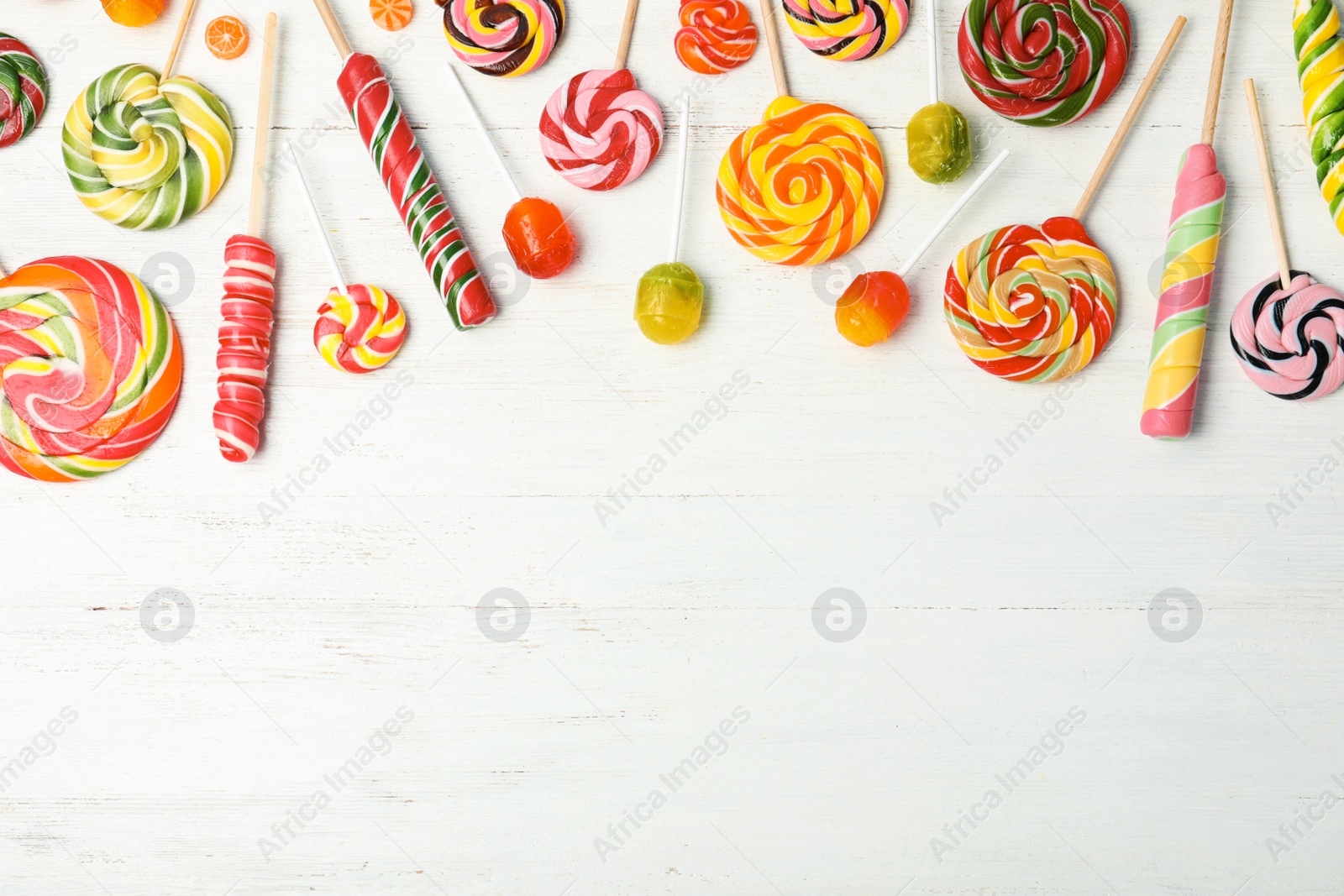 Photo of Different colorful candies and space for text on white wooden background, top view