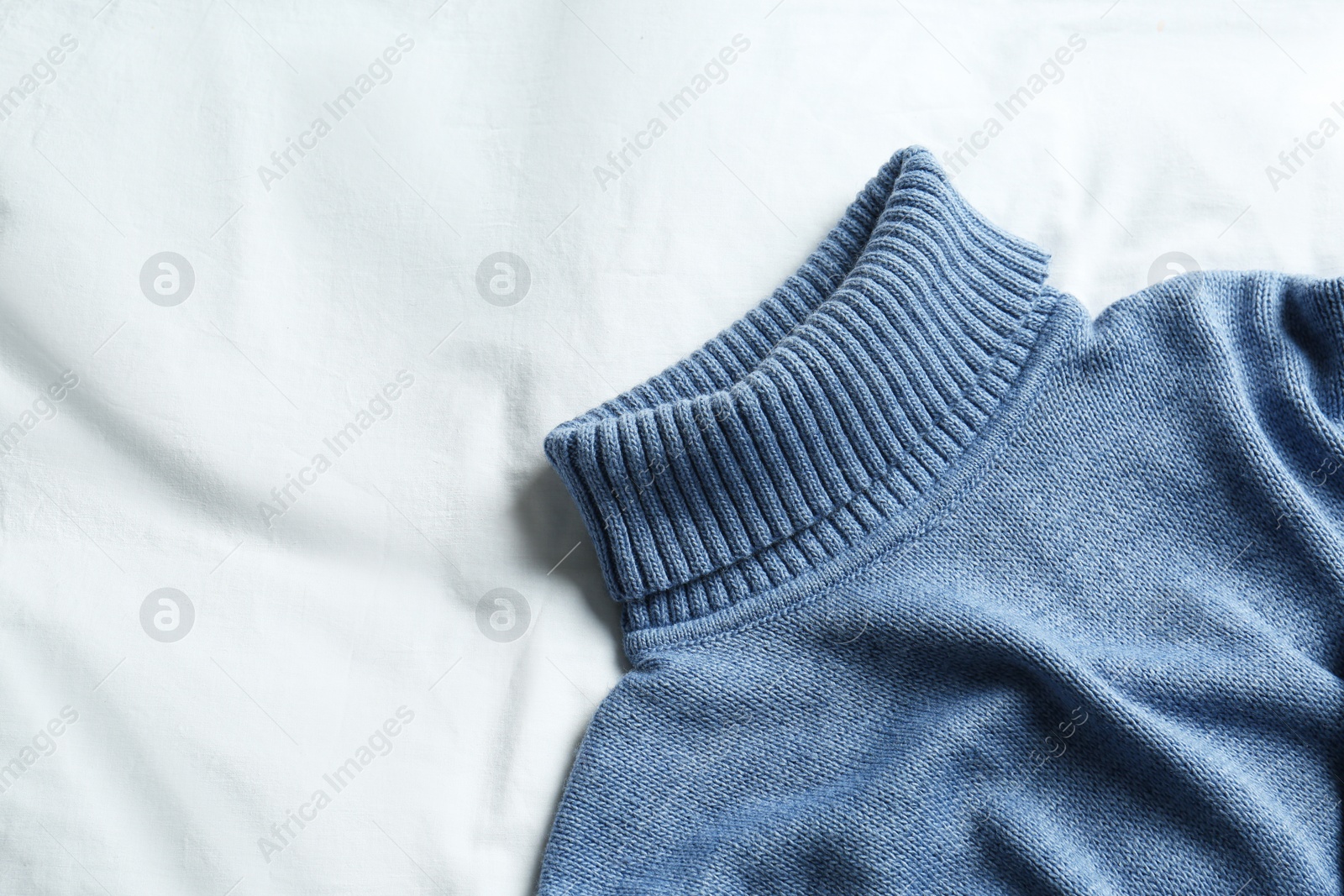 Photo of Stylish knitted sweater on white fabric, top view. Space for text