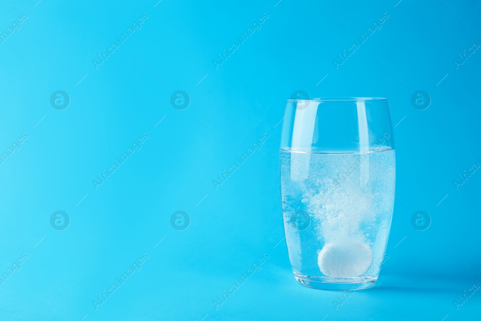 Photo of Glass of water with effervescent tablet on light blue background, space for text