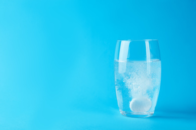 Photo of Glass of water with effervescent tablet on light blue background, space for text